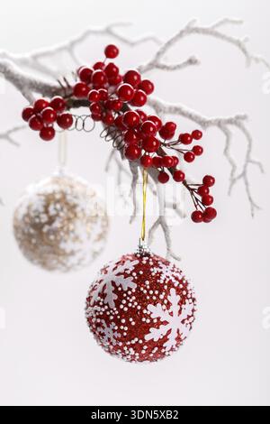 Rote Beeren auf verschneiten Zweig mit hängenden Weihnachtskugeln vertikale Stockfoto