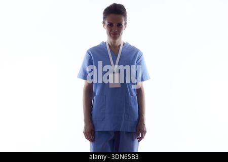 Hintergrundbeleuchtetes Porträt einer anonymen Krankenschwester oder eines medizinischen Fachpersonals, das blaue Peelings und ein Ausweisschild trägt, isoliert auf weißem Hintergrund mit Kopie sp Stockfoto