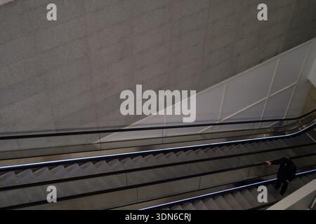 Ein einsamer Mann im dunklen Mantel steigt nachts in einer U-Bahn-Station in New York City auf eine lange, schmale Rolltreppe. Stockfoto