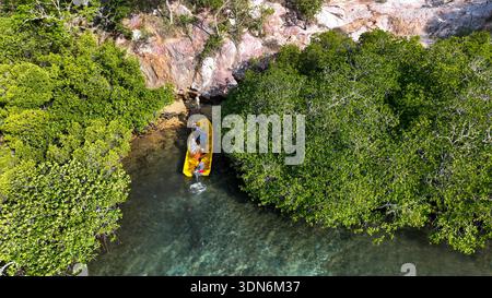 Das hellgelbe Boot gleitet über klares, flaches Wasser in Richtung eines schmalen Mangrovenkanals neben einer zerklüfteten, bunten Klippe. Stockfoto