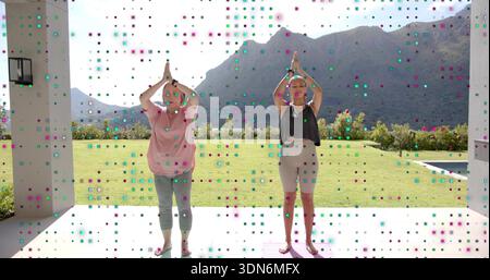 Üben von Mutter und Tochter in rosafarbenen dunklen Tops und beten auf der Terrasse mit Yoga-Matten Stockfoto