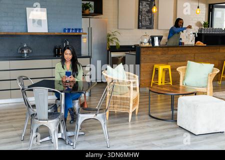 MittelErwachsene indische Frau, die am Glastisch in der modernen Coffee Shop Lounge mit Smartphone sitzt Stockfoto