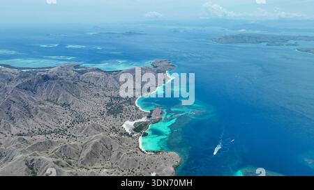 Bootswege schlängeln sich durch türkisfarbene Buchten entlang der trockenen Hügel von Komodo und enthüllen unberührte Strände, die zwischen Inselketten eingebettet sind. Stockfoto