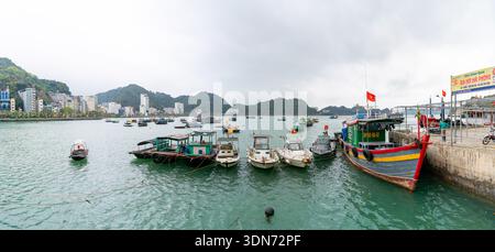 Eine lebendige Szene in Vietnam, mit farbenfrohen Booten, die an einem Pier vor dem Hintergrund einer Stadt und grüner Hügel anlegen. Vietnam, 10. 10. 2025 Stockfoto