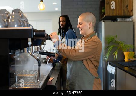 Verschiedene Barista-Kollegen bedienen die Espressomaschine hinter dem Coffee Shop mit Dampfdüse Stockfoto