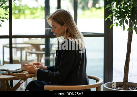 Entspannte Geschäftsfrau mit Smartphone, während sie in der Mittagspause von der Arbeit am Kaffeetisch sitzt. Stockfoto