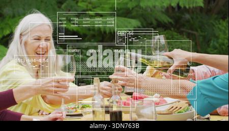 Lachende Gruppe von sechs Erwachsenen, die Weingläser an einem hölzernen Picknicktisch im Hinterhof anklickend, mit AR-Überzug Stockfoto