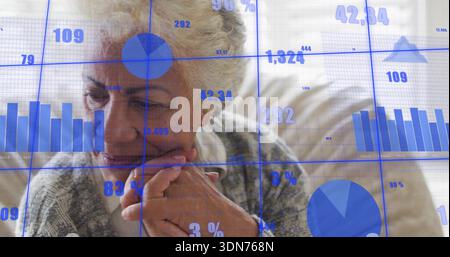 Reflektierende ältere Frau, die zu Hause die Hände auf der Couch festlegt, graue Strickjacke, Datenüberlagerungen trägt Stockfoto