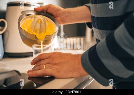 Nahaufnahme von Händen, die während einer entspannten Morgenroutine frischen Saft in ein Glas in einer Küche gießen. Vorstellung von Alltagsgewohnheiten, einfachem Lebensstil und Stockfoto