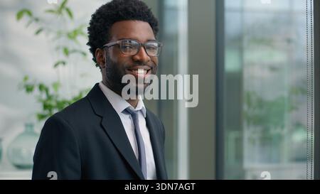 Afroamerikanischer Mann Geschäftsmann männlicher Geschäftsmann schaut im Fenster lächelnd auf Kameraprait im Büro Arbeitgeber Manager Firma CEO Investor Stockfoto