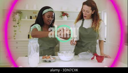 Zwei Frauen, die in der weißen Küche Teig vorbereiten, Olivenschürzen tragen, Schüssel, Schneebesen, Eier benutzen, Becher Stockfoto