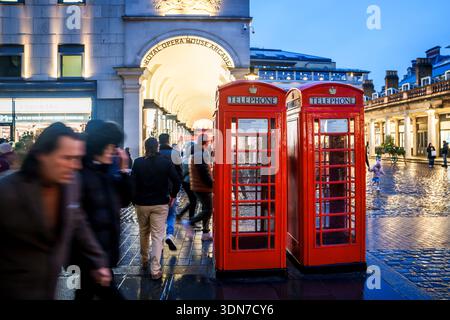 LONDON, GROSSBRITANNIEN. Februar 2025. Leute, die an der Arkade des Royal Opera House und den traditionellen roten Telefonzellen in der Abenddämmerung vorbeilaufen. Stockfoto