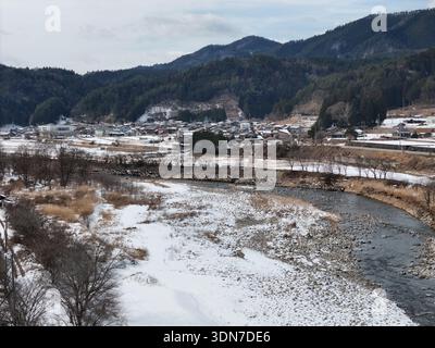 Eine schneebedeckte Landschaft mit einem Fluss, der durch sie fließt. Der Fluss ist von Bäumen und Häusern umgeben. Die Szene hat eine friedliche und ruhige Stimmung Stockfoto