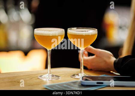Zwei gelbe Cocktails in Coupé-Gläsern stehen auf einer hölzernen Bartheke im Barinneren. Stockfoto