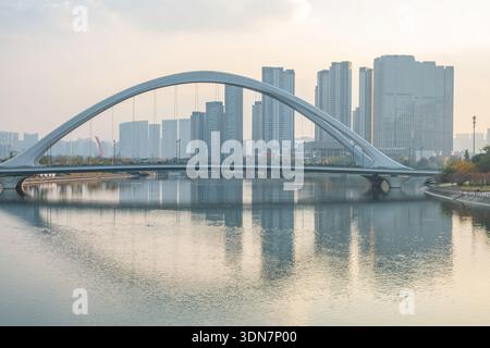 Moderne Bogenbrücke über einen ruhigen Fluss mit moderner Skyline bei Sonnenuntergang in Chengdu, Provinz Sichuan, China. Moderne städtische Infrastruktur und Stockfoto