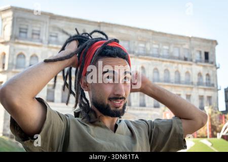 Ein Mann mit Dreadlocks, der ein Stirnband trägt und in die Stadt hinaufblickt Stockfoto