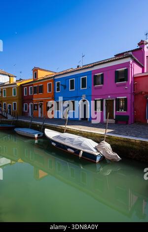 Farbenfrohe Häuser säumen einen Kanal mit Booten, die in einem sonnigen, ruhigen Viertel angedockt sind. Burano, Lagune Venetian, Italien Stockfoto