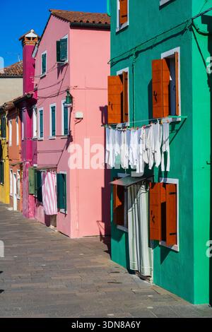 Farbenfrohe Gebäude mit trocknender Kleidung auf einer sonnigen Straße in einem lebhaften Viertel. Burano, Lagune Venetian, Italien Stockfoto