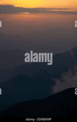 Sonnenuntergang über einer nebeligen Bergkette mit Schichten von Gipfeln und Wolken in den Fernen Bergen von Ta Xua, Bac Yen District, Son La, Vietnam Stockfoto