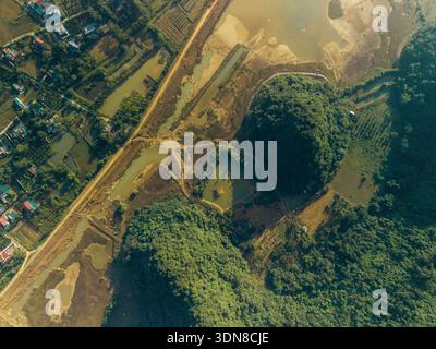 Blick aus der Vogelperspektive auf üppige grüne Hügel und gewundene Schotterstraßen in der Nähe von verstreuten Gewässern. Yen Thuy District, Hoa Binh, Vietnam Stockfoto