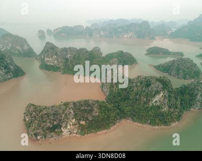 Blick aus der Vogelperspektive auf üppig grüne Inseln mit felsigen Klippen in einem nebeligen, ruhigen, blau-grünen Meer. Lan Ha Bay, Cat Ba, Vietnam Stockfoto