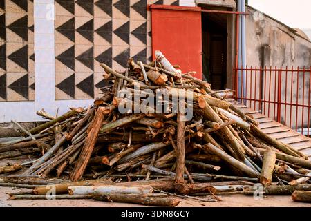 Ein Stapel von Baumstämmen, die vor einer geometrisch gemusterten Gebäudewand gestapelt sind. Kigali, Ruanda Stockfoto