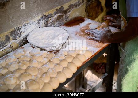 Mit den Händen den Teig auf einem mit Mehl bedeckten Holztisch mit Reihen von Teigkugeln bearbeiten. Kigali, Ruanda Stockfoto