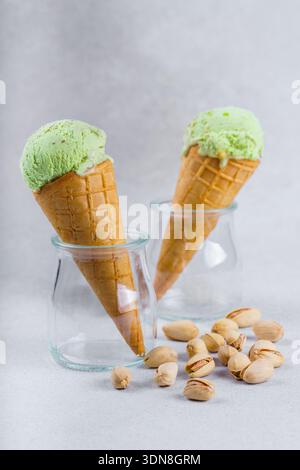 Zwei Pistazien-Eiskegel mit grünen Schaufeln in Glasgläsern mit verstreuten Pistazien-Nüssen auf hellem, strukturiertem Hintergrund. Frischer, kalter Sommer Stockfoto
