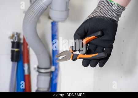 Nahaufnahme einer professionellen Hand, die wichtige Zange für die Sanitäranlage unter einem Waschbecken präzise greift und einen fachkundigen Heimservice veranschaulicht Stockfoto
