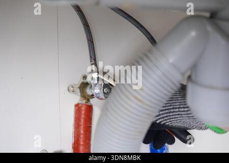 Nahaufnahme einer professionellen Hand, die ein Chrom-Absperrventil mit flexiblen Wasserschläuchen und einem weißen Abflussrohr festzieht, was für HOM steht Stockfoto
