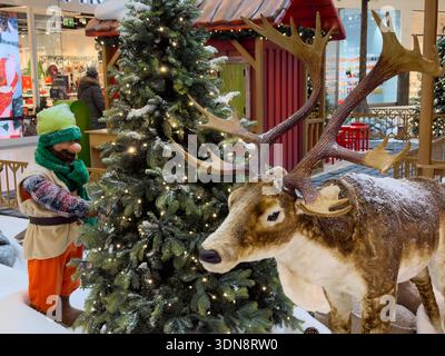 Eine lebhafte Weihnachtsszene im Innenbereich mit einem bezaubernden Zwerg neben einem beleuchteten Baum und einem majestätischen, schneebedeckten Rentier, perfekt für saisonale Retai Stockfoto