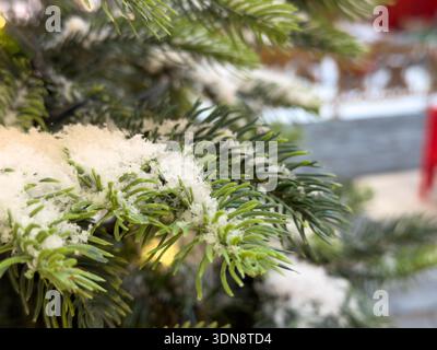Nahaufnahme eines üppig grünen künstlichen Kiefernzweigs, der mit strahlendem weißem Schnee bestäubt ist und das Wesen der Weihnachtszeit perfekt einfängt Stockfoto