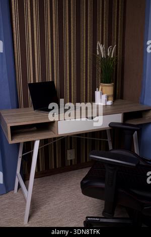 Moderner Schreibtisch mit Laptop, Stuhl und gestreiftem Wandhintergrund Stockfoto