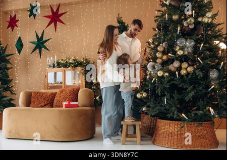 Einen Baum dekorieren. Eine glückliche Familie mit Kind, die zu Hause Weihnachten feiert. Stockfoto