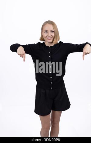 Selbstbewusste Frau in schwarzem Kleid, die im Studio nach unten zeigt Stockfoto