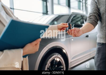 Geschäftsleute in formeller Kleidung überreichen einem Kunden in einem modernen Ausstellungsraum Autoschlüssel und zeigen dabei den Kaufprozess und den Stockfoto