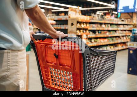 Die Person schiebt einen Einkaufswagen durch einen Gang des Lebensmittelgeschäfts, der mit verschiedenen Produkten gefüllt ist, mit leuchtenden Farben und organisierten Regalen, Kreatin Stockfoto