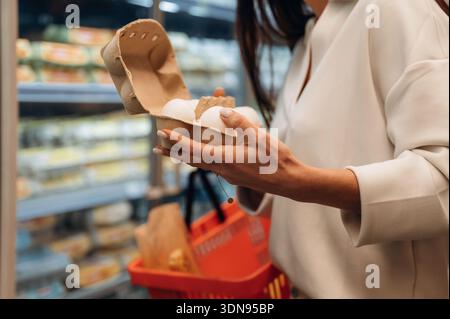 Die weibliche Käuferin hält einen Eierkarton in einem Gang eines Lebensmittelgeschäfts, umgeben von bunten Lebensmitteln und einem Warenkorb, der alles hervorhebt Stockfoto