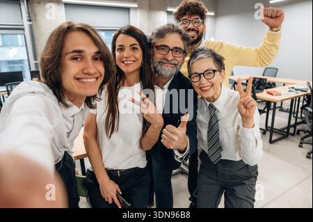 Verschiedene Gruppen von Fachleuten posieren gerne für ein Selfie in einem modernen Bürobereich und heben Teamarbeit und Zusammenarbeit zwischen Kollegen in hervor Stockfoto
