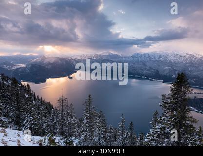 Wintersonnenaufgang mit Pastellfarben am Himmel über dem Walchensee mit den schneebedeckten zerklüfteten Bergen im Hintergrund. Stockfoto