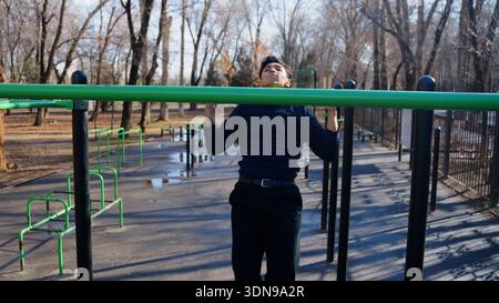 Junger Mann, der auf dem Sportplatz im Freien Pull-ups macht Stockfoto