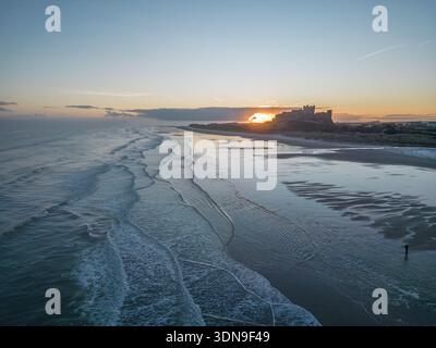 Das berühmte Bamburgh Castle an einem eiskalten Morgen bei Sonnenaufgang, neben dem schneebedeckten Strand in Northumberland, England, von Drohnen eingenommen. Stockfoto