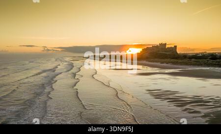 Das berühmte Bamburgh Castle an einem eiskalten Morgen bei Sonnenaufgang, neben dem schneebedeckten Strand in Northumberland, England, von Drohnen eingenommen. Stockfoto