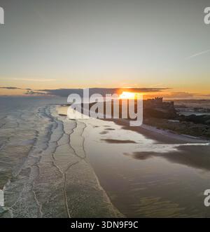 Das berühmte Bamburgh Castle an einem eiskalten Morgen bei Sonnenaufgang, neben dem schneebedeckten Strand in Northumberland, England, von Drohnen eingenommen. Stockfoto