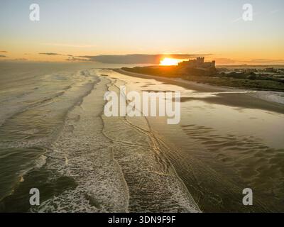 Das berühmte Bamburgh Castle an einem eiskalten Morgen bei Sonnenaufgang, neben dem schneebedeckten Strand in Northumberland, England, von Drohnen eingenommen. Stockfoto