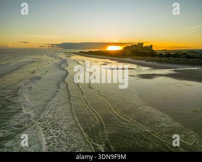 Das berühmte Bamburgh Castle an einem eiskalten Morgen bei Sonnenaufgang, neben dem schneebedeckten Strand in Northumberland, England, von Drohnen eingenommen. Stockfoto