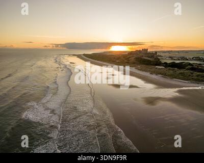 Das berühmte Bamburgh Castle an einem eiskalten Morgen bei Sonnenaufgang, neben dem schneebedeckten Strand in Northumberland, England, von Drohnen eingenommen. Stockfoto