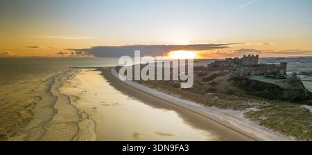 Das berühmte Bamburgh Castle an einem eiskalten Morgen bei Sonnenaufgang, neben dem schneebedeckten Strand in Northumberland, England, von Drohnen eingenommen. Stockfoto