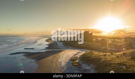Das berühmte Bamburgh Castle an einem eiskalten Morgen bei Sonnenaufgang, neben dem schneebedeckten Strand in Northumberland, England, von Drohnen eingenommen. Stockfoto