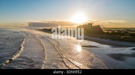 Das berühmte Bamburgh Castle an einem eiskalten Morgen bei Sonnenaufgang, neben dem schneebedeckten Strand in Northumberland, England, von Drohnen eingenommen. Stockfoto